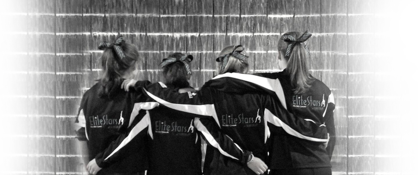 Four Elite Stars gymnasts in team jackets, arms around each other